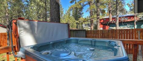 Un jacuzzi al aire libre con una terraza de madera y árboles de fondo.