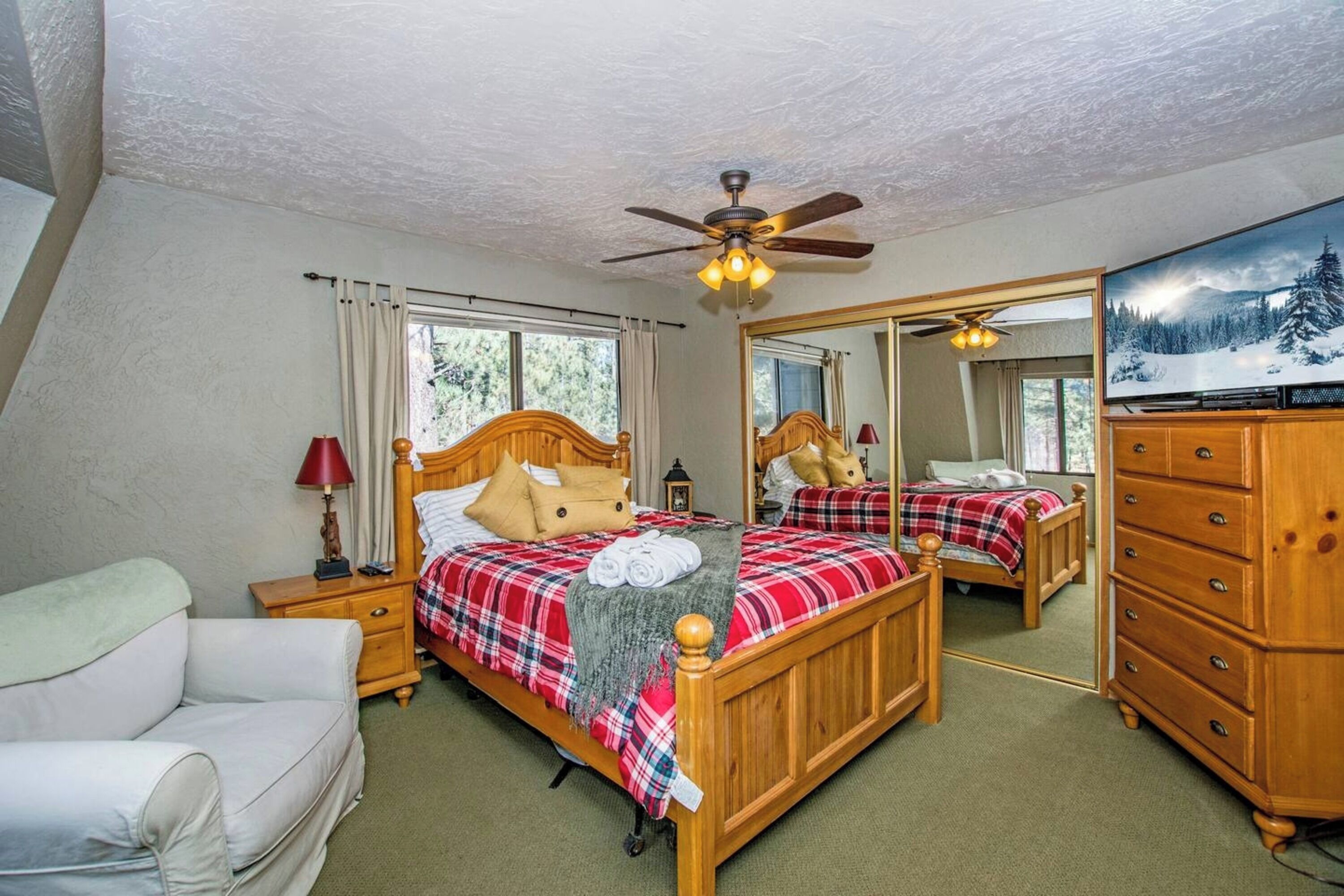 Une chambre à coucher avec deux lits en bois, un ventilateur de plafond, un grand miroir, une commode et un téléviseur.
