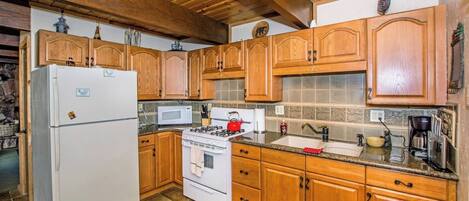 A kitchen with wooden cabinets, a refrigerator, stove, microwave, and a sink.