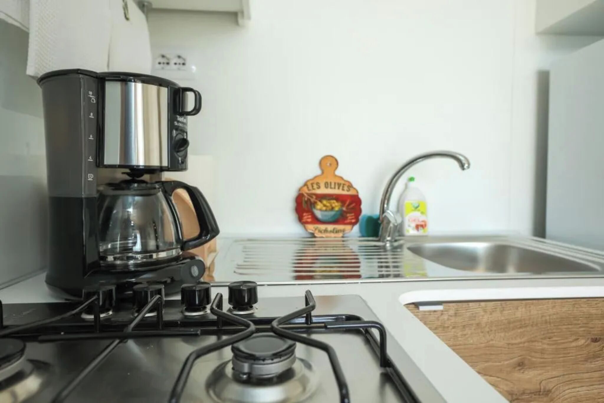 A kitchen with a coffee maker, a bottle of olive oil, and a sink.
