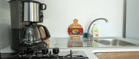 A kitchen with a coffee maker, a bottle of olive oil, and a sink.