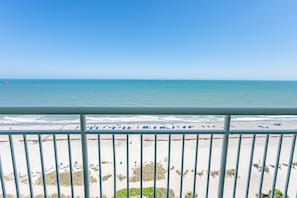 Uitzicht op een strand vanaf een balkon met een balustrade, zandstrand en zee.