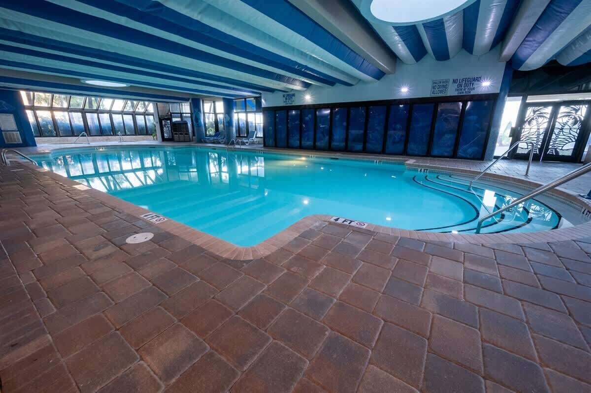 En inomhuspool med kristallklart blått vatten, omgiven av ett tegelgolv och stora fönster.