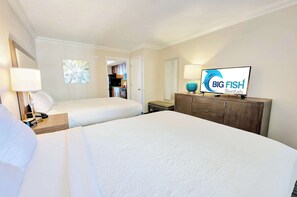 Une chambre d’hôtel avec deux lits, une commode en bois, un téléviseur affichant le logo de « BIG FISH Rentals », et une petite fenêtre donnant sur un arbre.