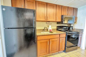 Une cuisine avec des meubles de rangement en bois, un réfrigérateur noir, un four à micro-ondes, un évier et une cuisinière.