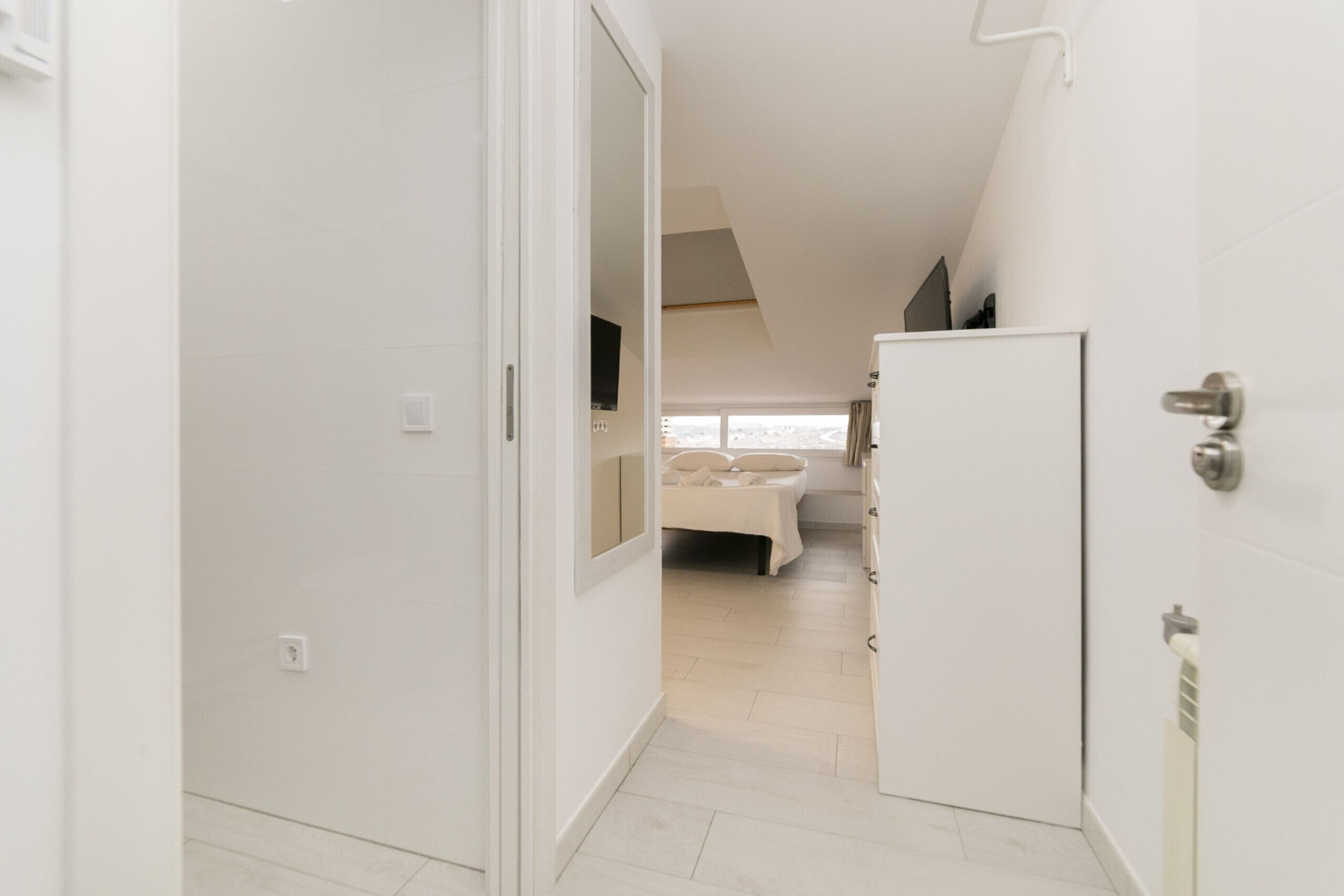 Un dormitorio moderno y minimalista con techo inclinado, cama con ropa de cama blanca y un amplio ventanal que proporciona luz natural.