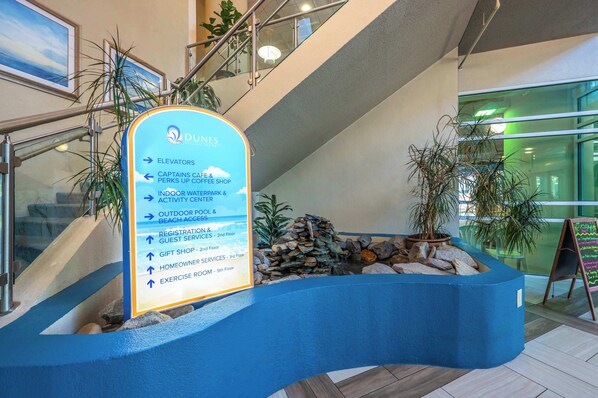 Zona de recepción de hotel con un cartel que enumera servicios como ascensores, un café Capitán, una cafetería, parques acuáticos interiores y exteriores, acceso a la playa, registro, servicios para huéspedes, una tienda de regalos, una sala para propietarios y un gimnasio.