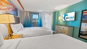 Ein Hotelzimmer mit zwei Betten, einem Fernseher, einem Schreibtisch und einem fensterbelaubten Fenster.