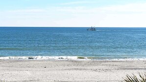 Ein Strand mit einem Boot in der Ferne, einem klaren Himmel und ruhiger See.