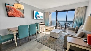 Ein modernes Hotelzimmer mit Essbereich, einer Couch, einem Fernseher und einem Balkon mit Blick.
