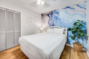 Een slaapkamer met een bed, een muurschildering, een potplant en een inloopkast.