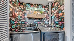 A laundry area with a wall decorated with a marine life theme, a wooden shelf, and a Samsung washing machine. - 2BR at Grand Palms Resort - Close to Beach (Myrtle Beach)