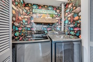 A laundry area with a wall decorated with a marine life theme, a wooden shelf, and a Samsung washing machine.