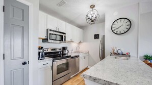 A modern kitchen with white cabinets, stainless steel appliances, a marble countertop, and a wall clock. - 2BR at Grand Palms Resort - Close to Beach (Myrtle Beach)
