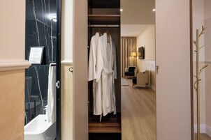 Habitación de hotel con bañera de mármol, perchero con batas blancas, suelo de madera, una silla negra y un perchero dorado.