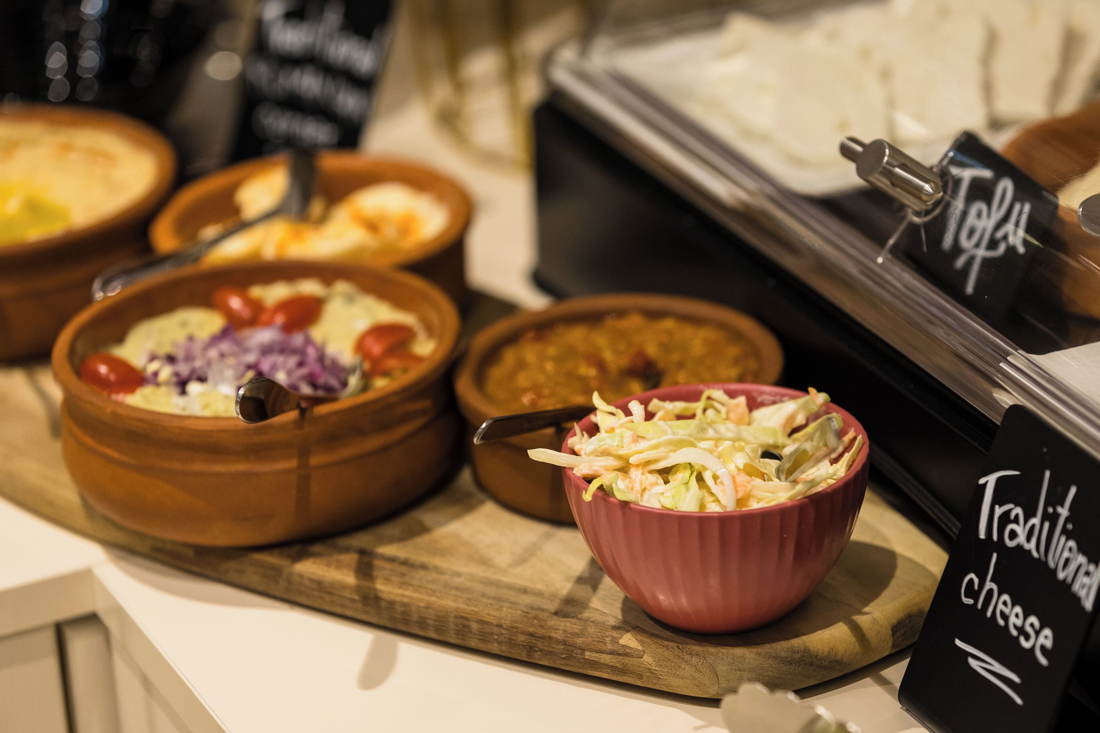 A buffet with various dishes including a bowl of coleslaw, a bowl of soup, and a dish labeled 'Traditional cheese'.