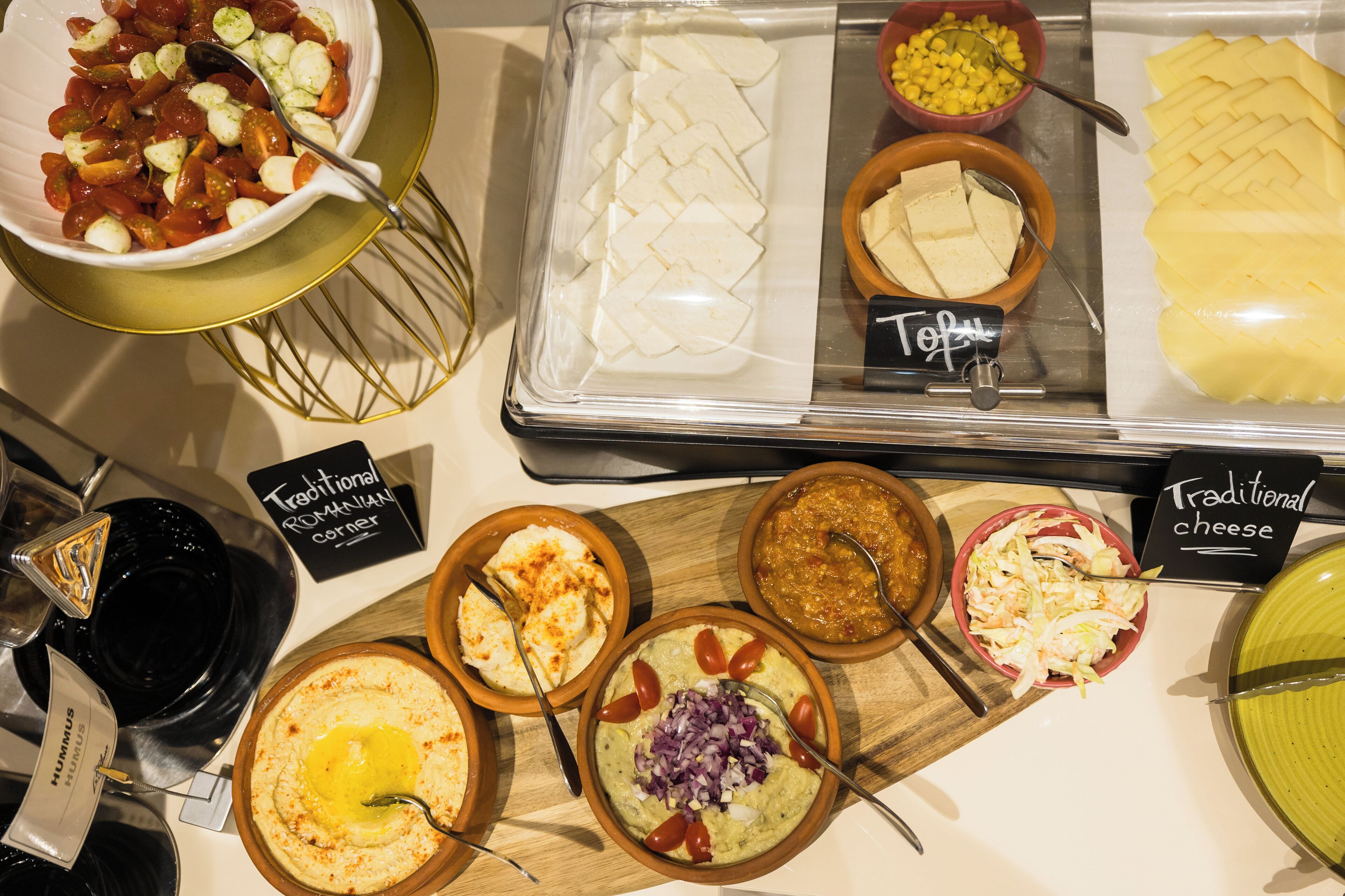 A variety of food items displayed in a buffet setting, including different types of cheese, hummus, and other dishes.