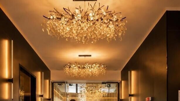 A woman walking down a hallway with a chandelier, potted plants, and a view into a dining area. - Le Blanc Cotroceni hotel (Bucharest)