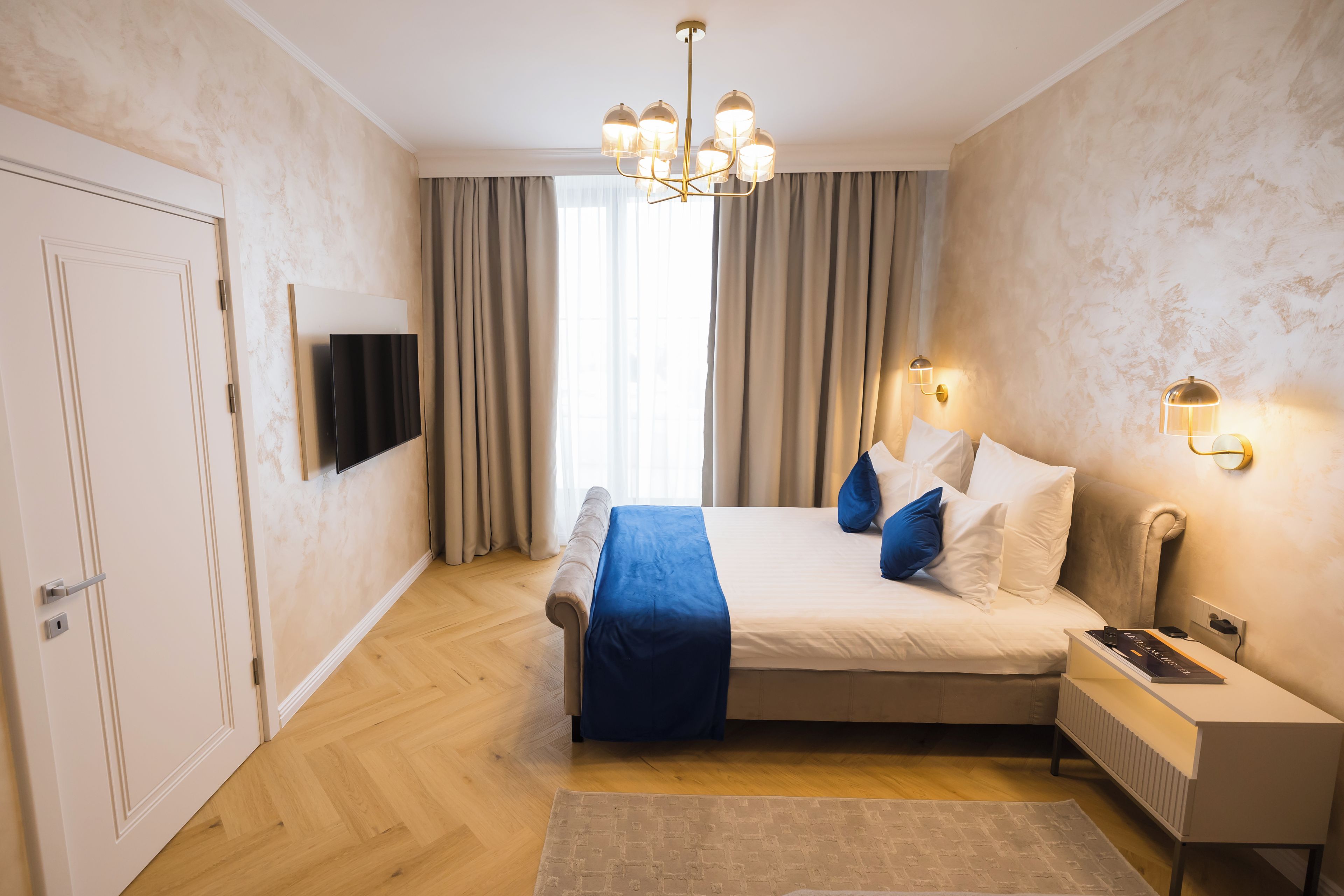 Quarto com cama, mesas de cabeceira, televisão e lustre.