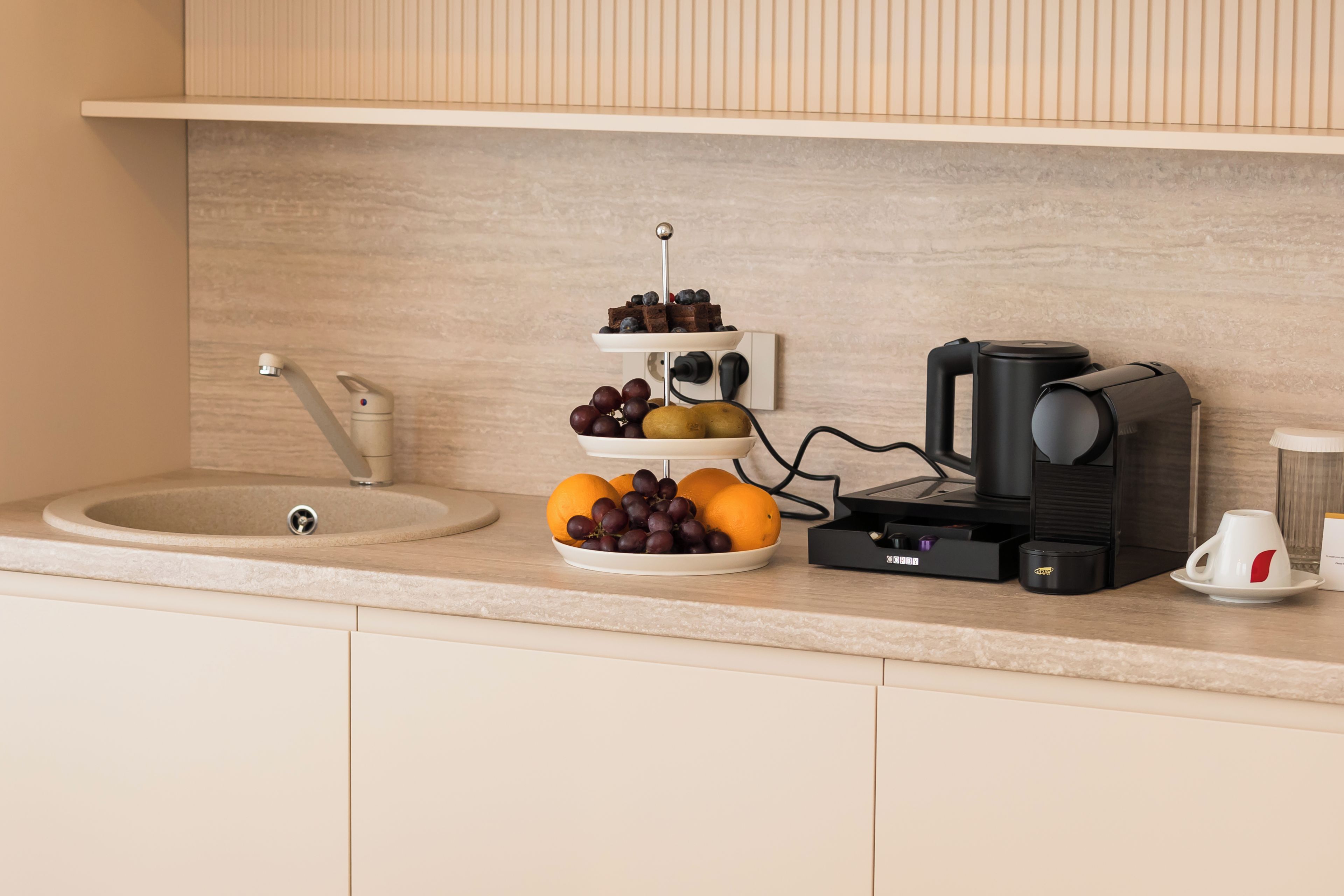 Una encimera de cocina con una cafetera, un frutero y un lavabo.