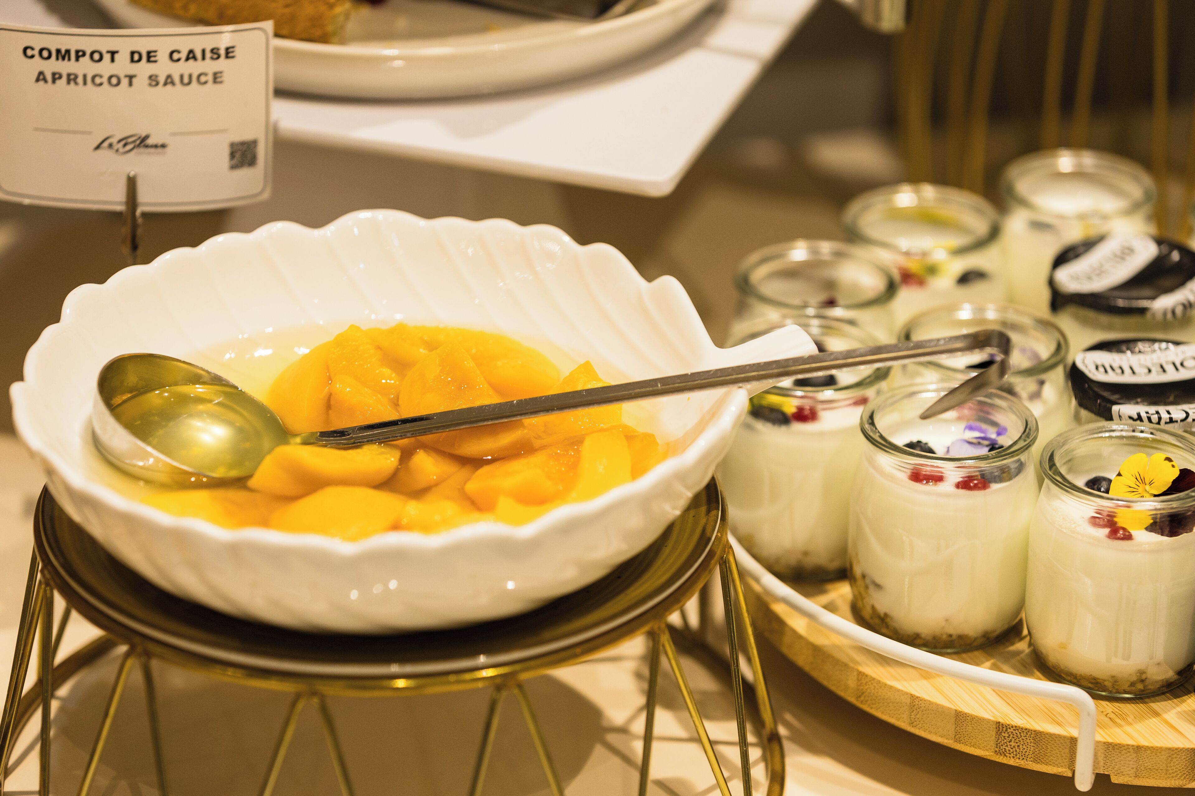 A dessert display with a bowl of peach compote and jars of yogurt parfaits.