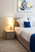 A neatly made bed with white and blue bedding, a bedside lamp, and a small nightstand.