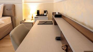 Una habitación de hotel con una cama, un escritorio con lámpara, una cafetera y un control remoto.