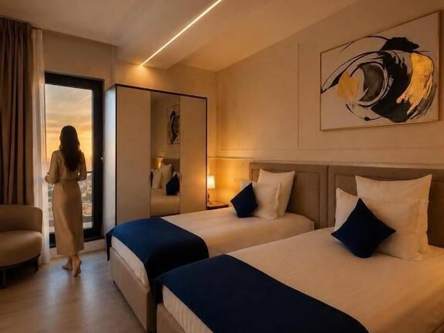 A hotel room with two beds, a sitting area, a large window, and a painting on the wall.