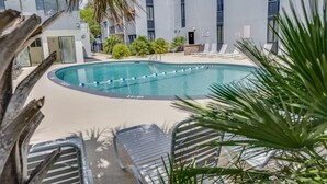 A swimming pool with lounge chairs and palm trees, surrounded by a building with large windows. - 2BR Holiday Towers, Newly Remodeled, Balcony, Pool (Myrtle Beach)