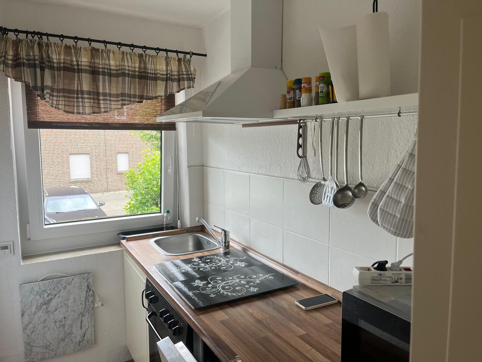 Eine Küche mit Fenster, Spüle, Herd und hängendem Kochgeschirr.