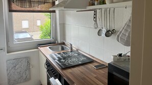 Una cocina con ventana, un lavamanos, una estufa y utensilios colgando.