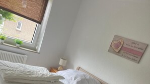 Una cama bien hecha con ropa blanca en una habitación con ventana, radiador y un letrero en la pared.