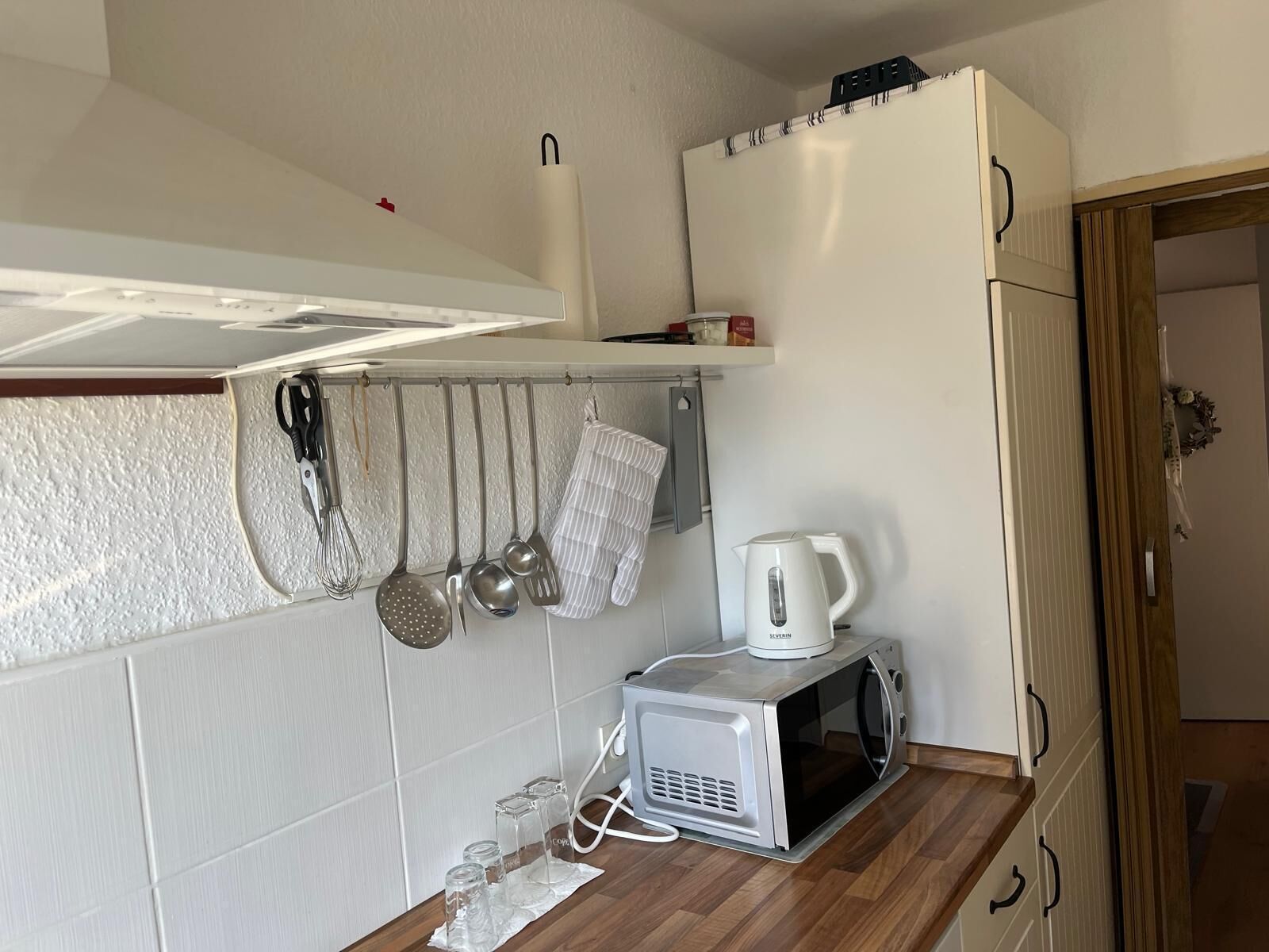 A compact kitchen with a microwave, kettle, and hanging utensils.