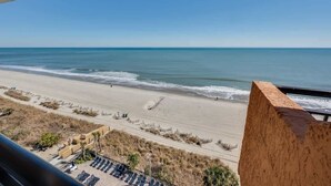 A beach view from a balcony with a clear sky, sandy beach, and a few umbrellas.