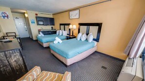 A hotel room with two beds, a desk, a chair, a microwave, and a TV.
