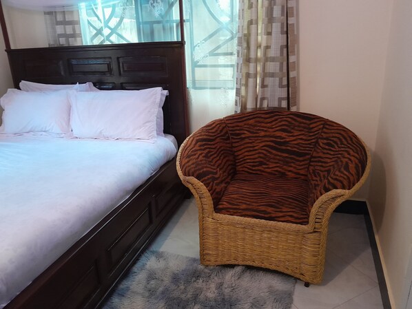 A bedroom with a bed, a wicker armchair, and a fluffy rug. - Stan Lodge Babati (Babati)