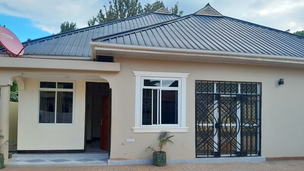 A single-story house with a beige exterior, a metal roof, and a gated entrance. - Stan Lodge Babati (Babati)