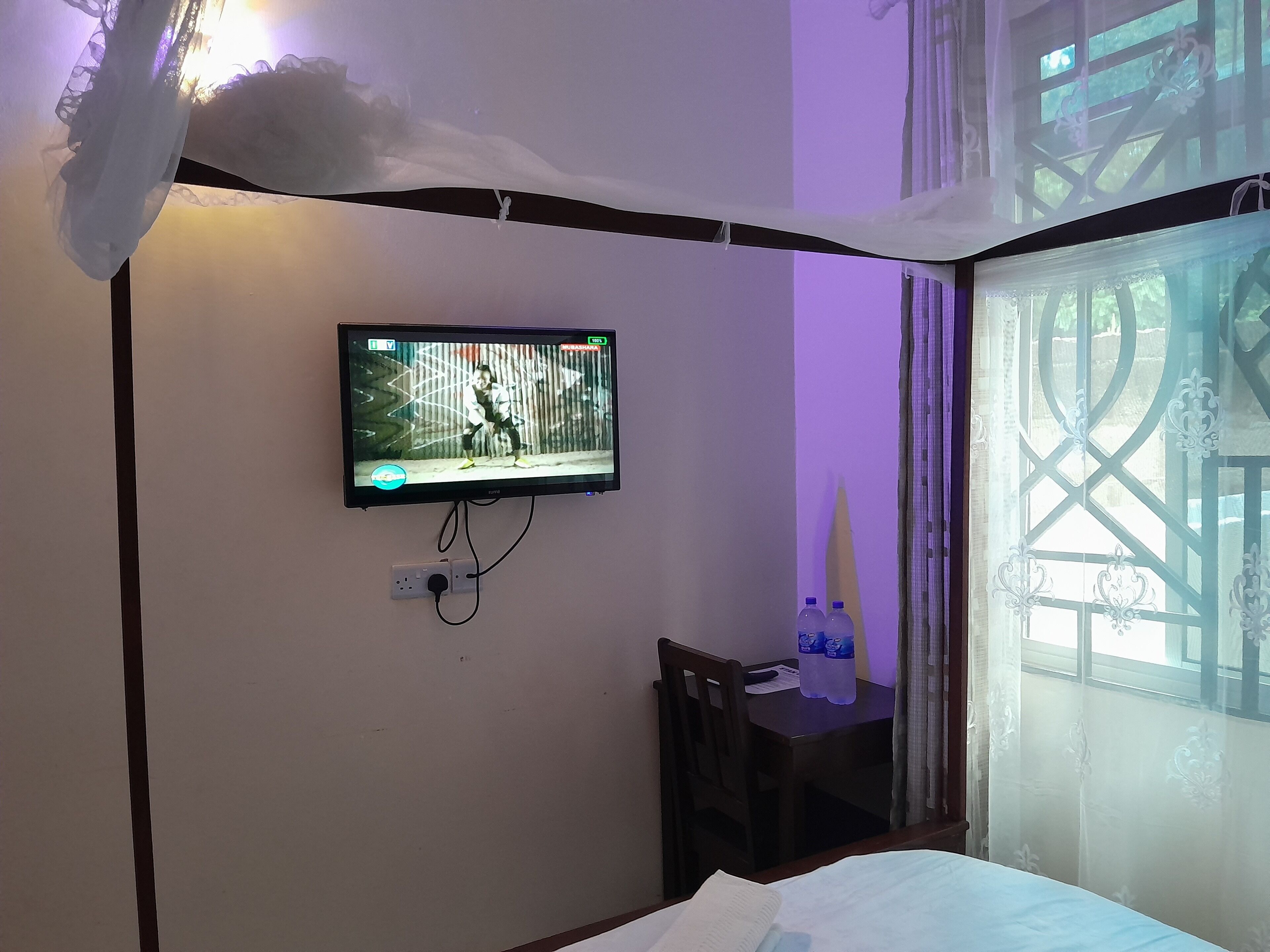 A room with a television mounted on the wall, a desk with a chair, and a bed.