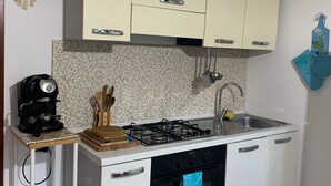 Une cuisine compacte avec des meubles blancs, une cuisinière à gaz, un évier et un petit plan de travail.