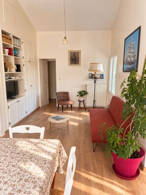 A living room with a sofa, a table with a floral tablecloth, a potted plant, a television, and a bookshelf. - House 100 meters from the ocean • Walks & Relaxation (Bretignolles-sur-Mer)