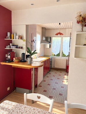 A compact kitchen with a red and white color scheme, a built-in oven, and a window providing natural light. - House 100 meters from the ocean • Walks & Relaxation (Bretignolles-sur-Mer)