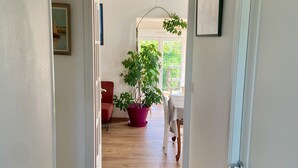 Een gang met een houten vloer, een potplant, een rode stoel en een eettafel met stoelen.