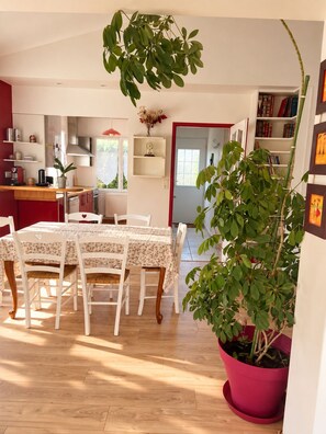 A dining area with a table set for four, surrounded by white chairs, a red door, and a bookshelf filled with books. - House 100 meters from the ocean • Walks & Relaxation (Bretignolles-sur-Mer)