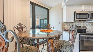 A dining area with a glass-top table, ornate chairs, a kitchen with modern appliances, and a sliding glass door leading to a balcony. - Newly Added - City Views - Private Maisons Sur Mer (Myrtle Beach)