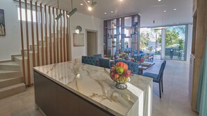 A modern kitchen with a marble island, a fruit bowl, and a dining area with blue chairs.