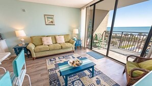 Een woonkamer met een bank, een salontafel en uitzicht op de oceaan vanuit een balkon.
