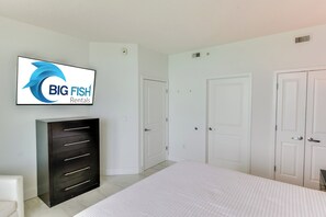 A bedroom with a bed, a wardrobe, a television displaying 'BIG FISH Rentals', and two doors.