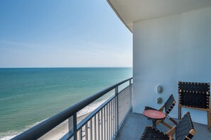 A balcony with a view of the sea, a table, and two chairs.