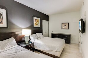A hotel room with two beds, a bedside table with a lamp, a dresser, and artwork on the walls.