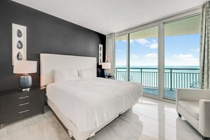 Une chambre dâhĂŽtel moderne, dotĂ©e dâun grand lit, dâune table de chevet, dâune lampe, dâune chaise et dâun balcon offrant une vue sur la mer.